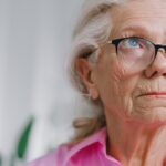 an elderly woman wearing glasses and a pink shirt gazing off in the distance